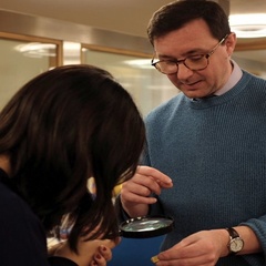 Photo of a student examining a tiny book, held out by the Librarian Jack Nixon, under a microscope,. 
