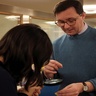 Photo of a student examining a tiny book, held out by the Librarian Jack Nixon, under a microscope,. 