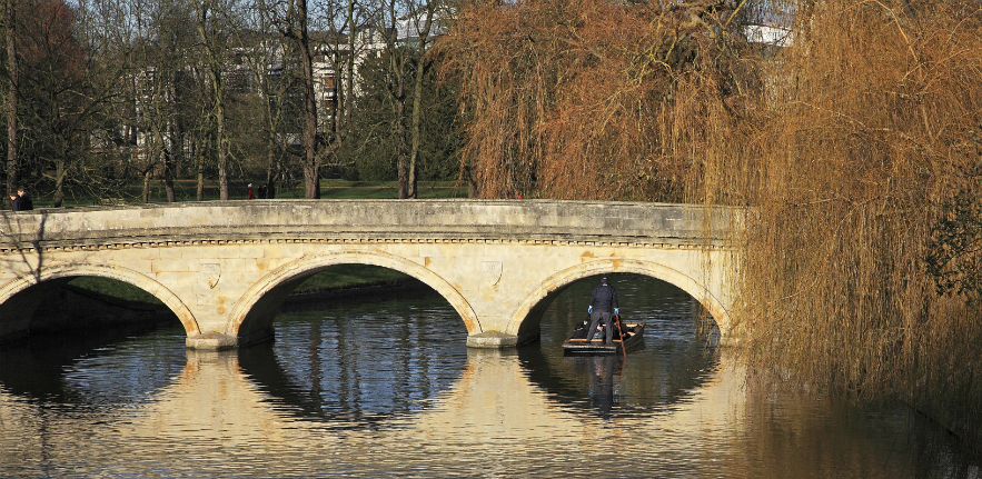 Steering a punt under a stone bridge on the river Cam, in autumn